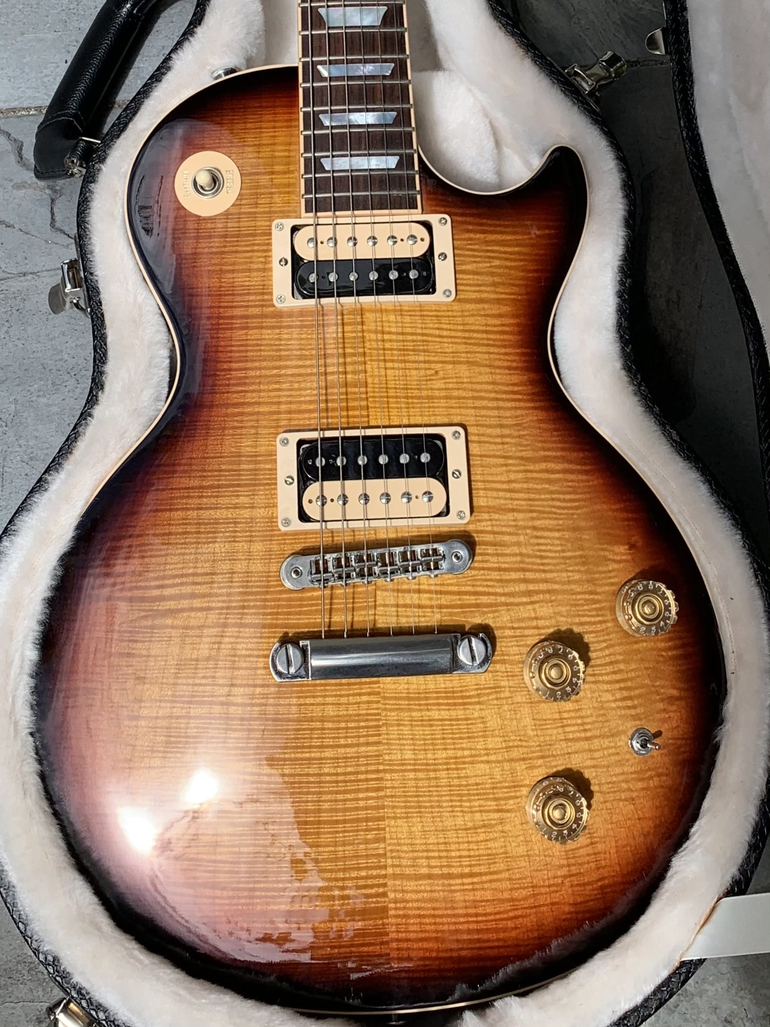 Sunburst electric guitar in open plush case. Rich wood grain, chrome hardware, light reflections. Stone background.
